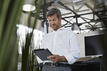 Überraschender Geschäftsmann im Büro mit Blick auf ein digitales Tablet - PDF000989