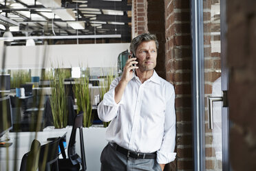 Geschäftsmann im Büro mit Smartphone und Blick aus dem Fenster - PDF000997