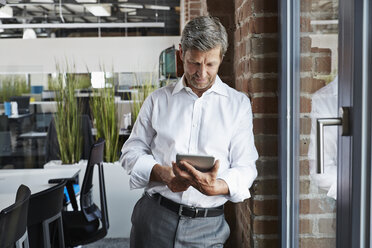 Businessman in office looking at digital tablet - PDF000994