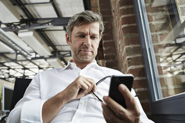 Geschäftsmann im Büro schaut auf sein Smartphone - PDF001010