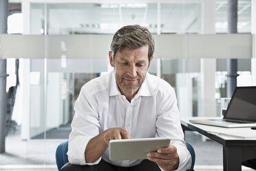Businessman in office looking at digital tablet - PDF001018