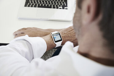 Businessman in office looking at smartwatch - PDF001068