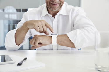 Geschäftsmann im Büro mit Blick auf eine Smartwatch - PDF001069