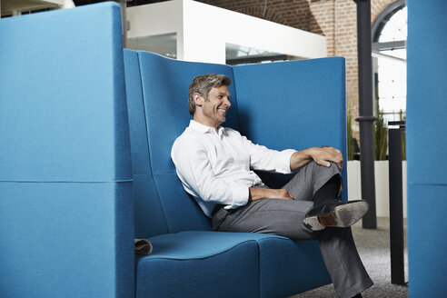 Smiling businessman sitting in conversation pit in office - PDF001031