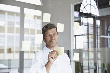 Businessman with sticky notes on glass pane in office - PDF001045