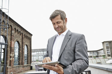 Lächelnder Geschäftsmann mit digitalem Tablet auf der Dachterrasse - PDF001051