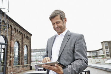 Smiling businessman using digital tablet on roof terrace - PDF001051