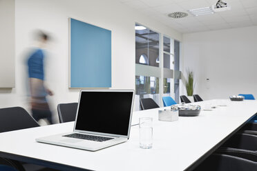 Laptop on conference table with blurred businessman in the background - PDF001059