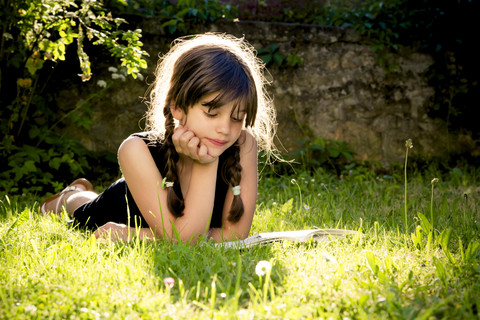 Girl lying on a meadow reading a book stock photo