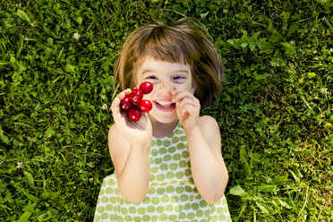 Lächelndes kleines Mädchen mit Kirschen auf einer Wiese liegend - LVF003500
