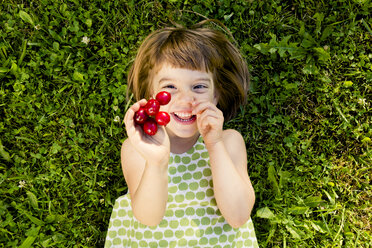 Smiling little girl with cherries lying on a meadow - LVF003500