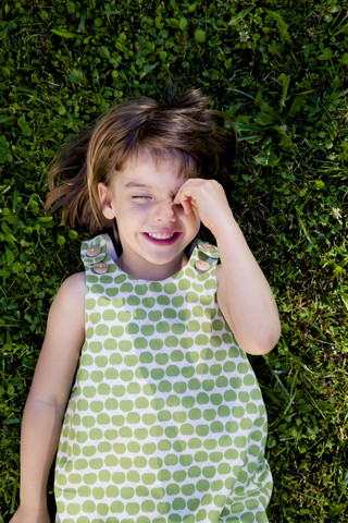 Lächelndes kleines Mädchen mit geschlossenen Augen auf einer Wiese liegend, lizenzfreies Stockfoto
