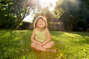 Little girl wearing cherries sitting on a meadow at backlight - LVF003505