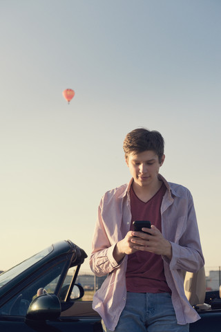 Teenager with smartphone leaning at convertible car stock photo