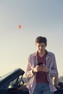 Teenager with smartphone leaning at convertible car - MSF004631