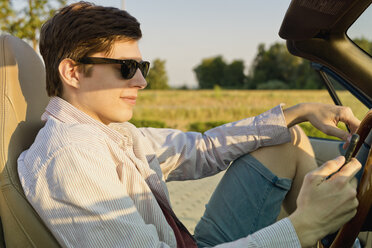 Teenager with sunglasses looking at his smartphone in a convertible car - MSF004632