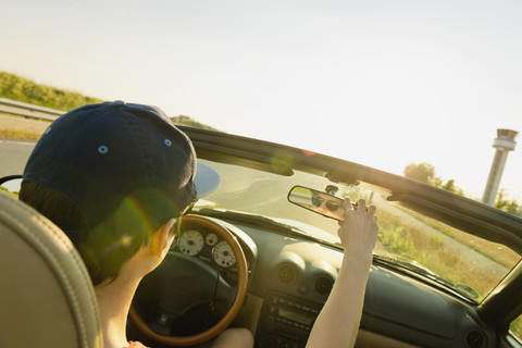 Teenager, der in einem Cabrio fährt und den Rückspiegel verstellt, lizenzfreies Stockfoto