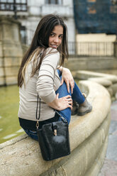 Spain, Oviedo, young woman sitting on the rim of a fountain in the old town - MGOF000287