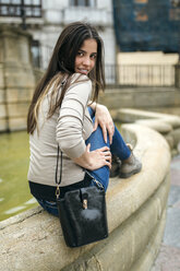 Spanien, Oviedo, junge Frau sitzt auf dem Rand eines Brunnens in der Altstadt - MGOF000287