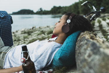 Relaxed young woman with headphones by the riverside - UUF004755