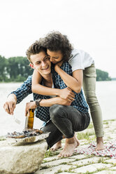 Glückliches junges Paar beim Grillen am Flussufer - UUF004765