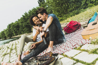 Happy young couple having a barbecue by the riverside - UUF004767