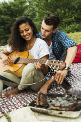 Entspanntes junges Paar spielt Gitarre und grillt im Freien - UUF004768