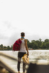 Junger Mann steht am Flussufer und hält eine Gitarre - UUF004783