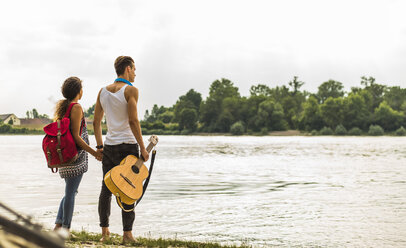 Young couple standing by the riverside with guitar - UUF004784