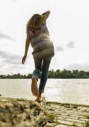 Young woman balancing on log by the riverside - UUF004803