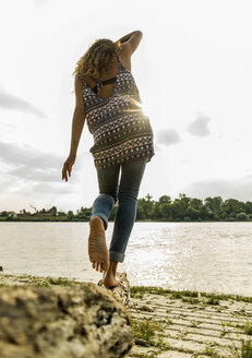 Junge Frau balanciert auf einem Baumstamm am Flussufer - UUF004803