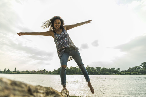 Junge Frau balanciert auf einem Baumstamm am Flussufer, lizenzfreies Stockfoto