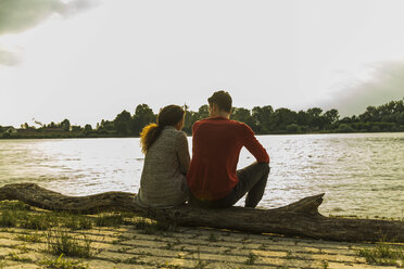 Junges Paar sitzt auf einem Baumstamm am Flussufer - UUF004810