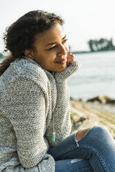 Smiling young woman sitting by the riverside - UUF004813