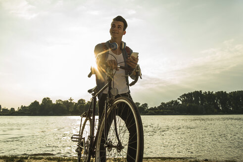 Young man with bicycle and cell phone by the riverside - UUF004817