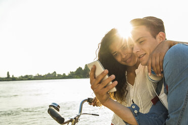 Young couple with bicycle and cell phone by the riverside - UUF004821