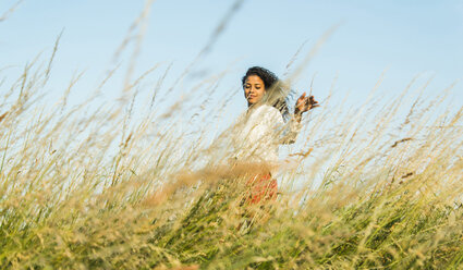 Langhaarige junge Frau in einem Feld mit hohem Gras - UUF004824