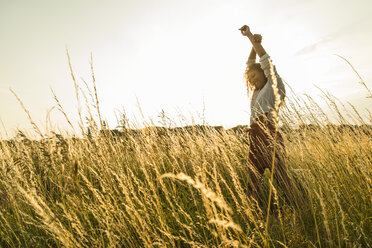 Young woman standing with raised arms in field with tall grass - UUF004830