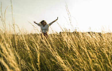 Young woman standing with outstretched arms in field with tall grass - UUF004831