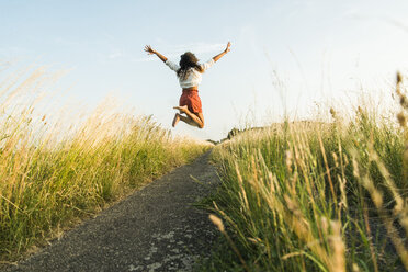 Enthusiastic young woman jumping on path in field - UUF004835