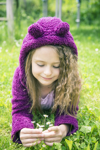 Mädchen liegt im Gras und pflückt Gänseblümchen, lizenzfreies Stockfoto