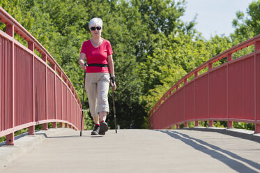 Ältere Frau beim Nordic Walking über eine Fußgängerbrücke - FRF000275