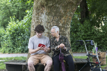 Ältere Frau sieht jungen Mann mit digitalem Tablet auf Parkbank an - SGF001671