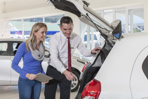 Car dealer showing new car to woman in showroom - ZEF006343