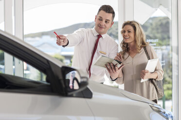 Car dealer showing new car to woman in showroom - ZEF006353