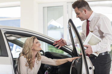 Car dealer showing new car to woman in showroom - ZEF006355