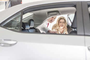 Car dealer showing new car to woman in showroom - ZEF006358