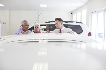 Car dealer showing new car to senior couple in showroom - ZEF006359