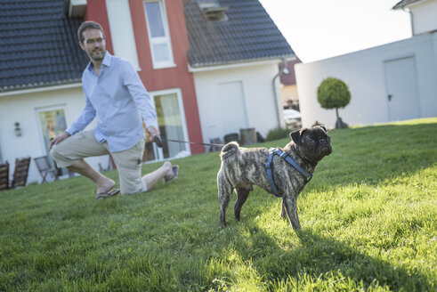 Mann unterrichtet Mops im Garten hinter dem Haus - PAF001442