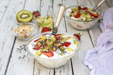 Strawberry kiwi yogurt with cereals, chia seeds, agave syrup in glass bowl on wood - SARF001914